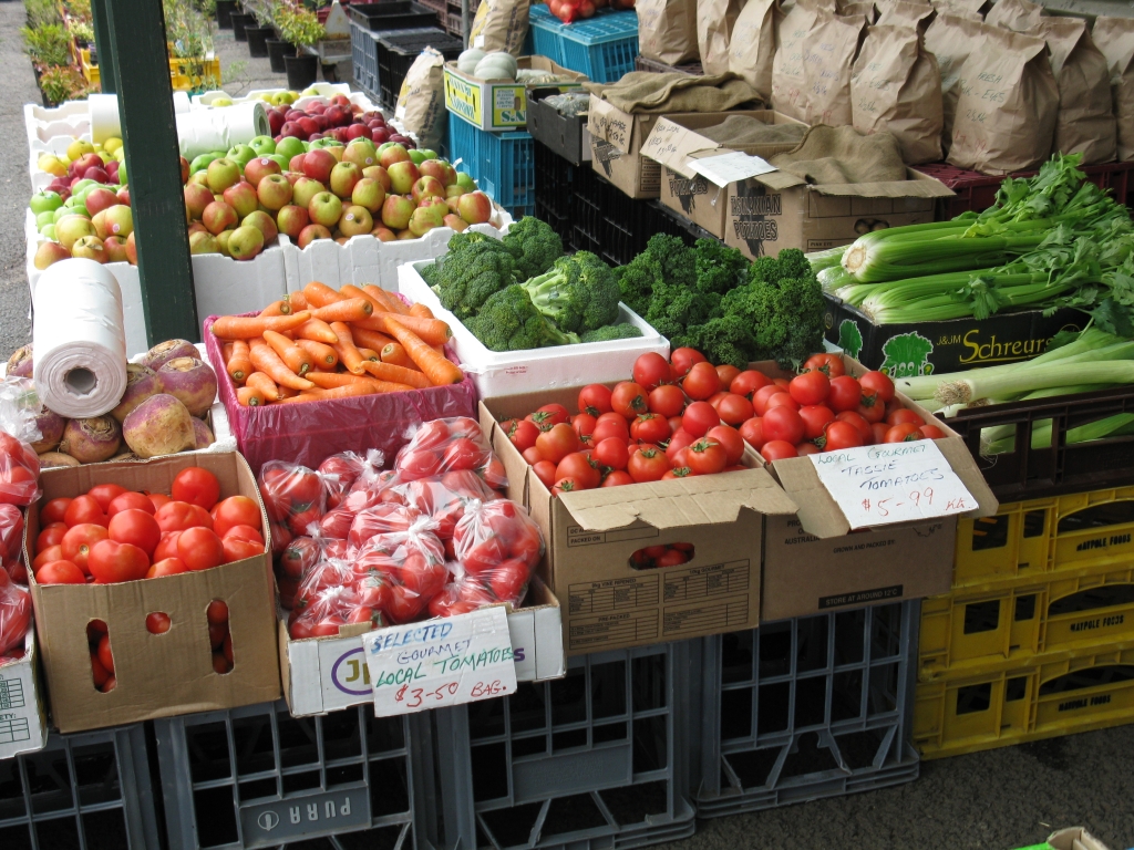 market stall displaying fresh fruit and vegetables including tomatoes, carrots, broccoli, celery, turnips, leek, potatoes and applese.