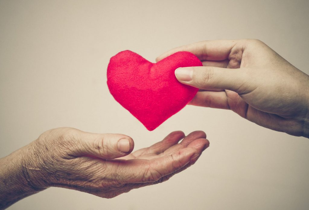 a picture of one persons hand holding a felt heart handing it over to the hand of another