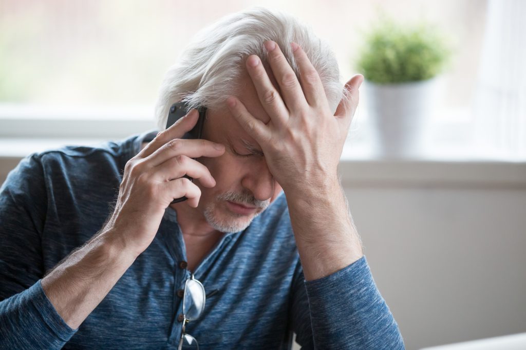 An older man looking stressed on the phone with a financial counsellor about bankruptcy options and unmanageable debt.