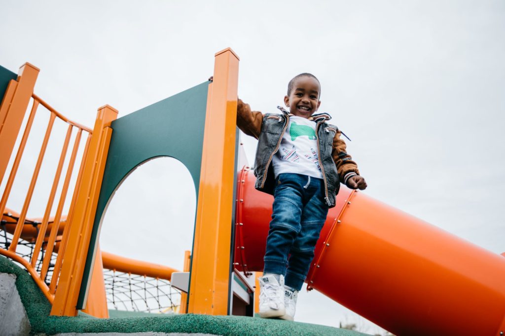 Young boy standing at the top of a slide looking down and smiling