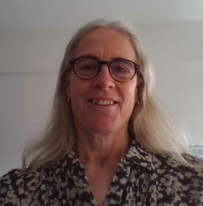 Susan has long grey hair, a floral shirt and is wearing glasses and smiling. 